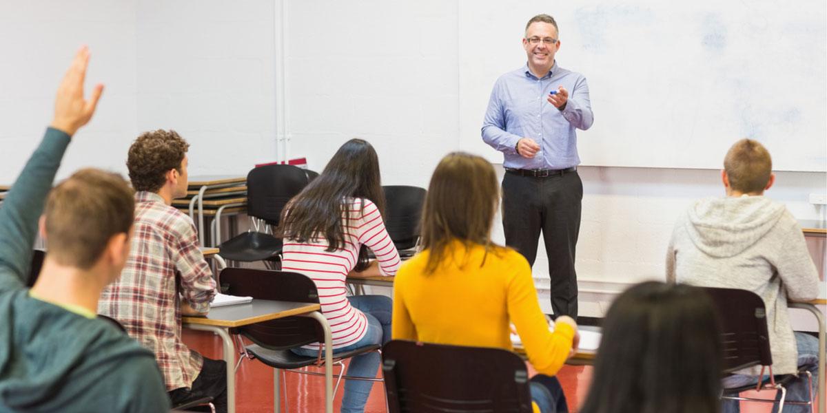 Male teacher stands in front of classroom.